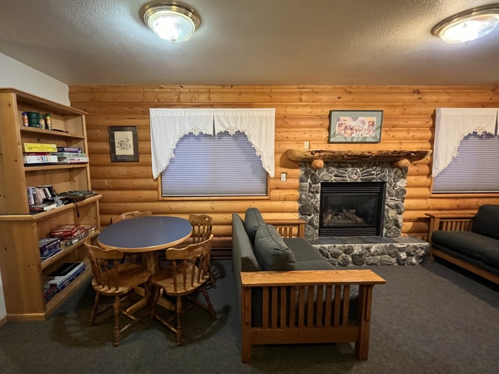 Cozy interior of a log cabin living room featuring a stone fireplace, wooden furniture, and a circular dining table with chairs.